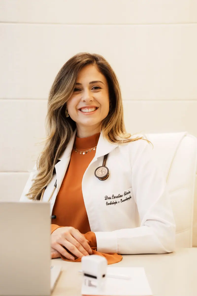 Dra. Caroline Silveira no consultório, com o jaleco bordado Cardiologia e Ecocardiografia